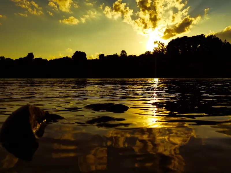 Zalazak sunca nad rekom, zlatni oblaci i staza svetlosti preko vode